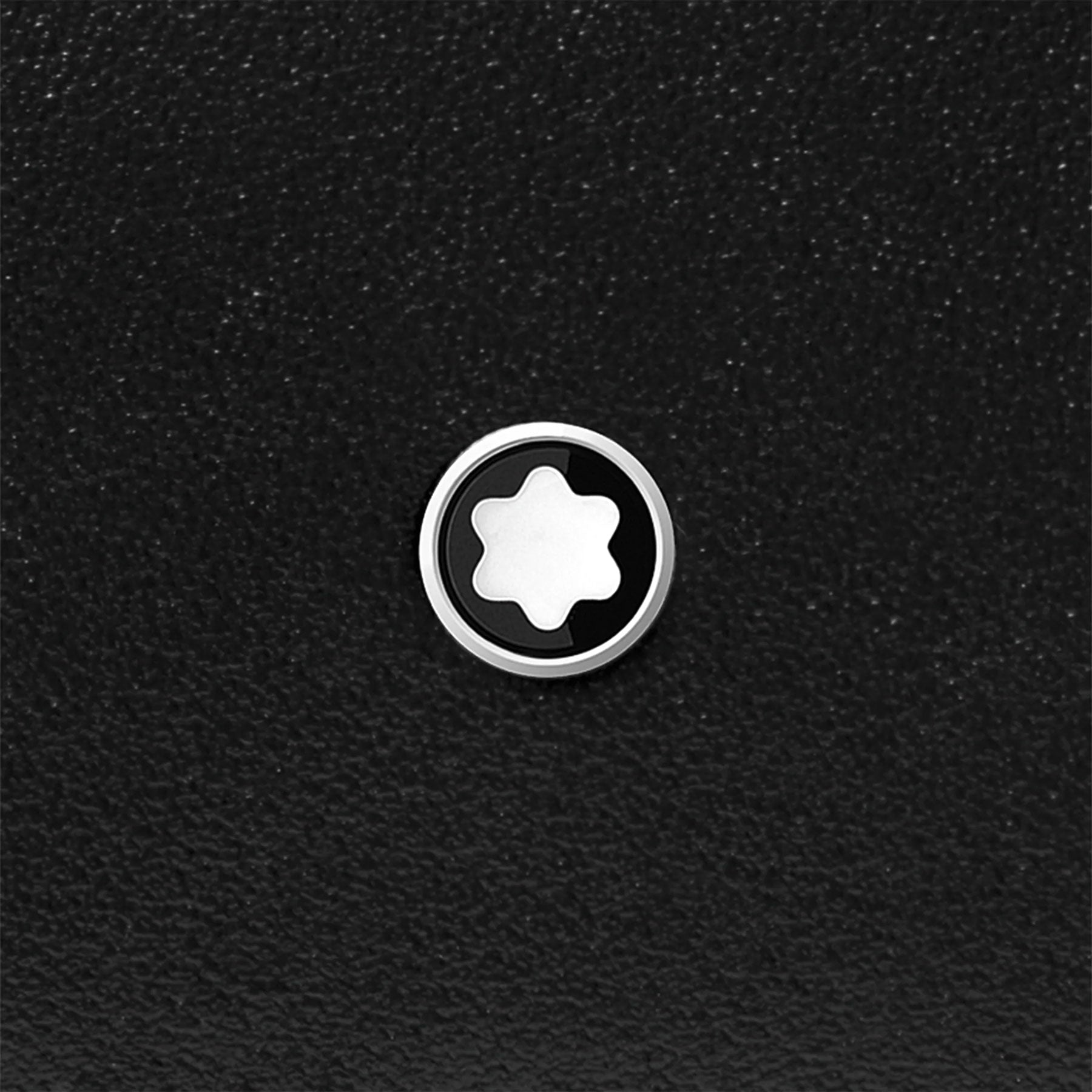 A circular logo with a white star-like design inside a black circle is prominently displayed against a textured black background, evoking the timeless sophistication of the Montblanc Meisterstück Compact Black Leather Wallet 6cc.