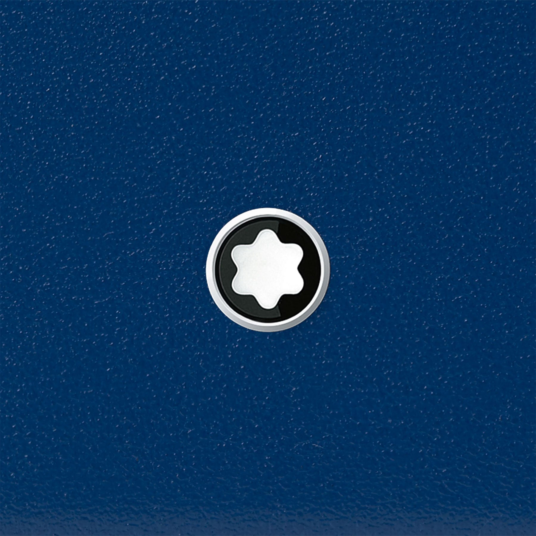 The image showcases the Montblanc Meisterstück Blue Leather Pocket 3CC Card Holder, featuring a textured blue surface. At its center is a circular emblem with a white star-like shape set against a black backdrop, all encased in a sleek silver ring. This striking design embodies the elegance of Montblanc's sophisticated craftsmanship.