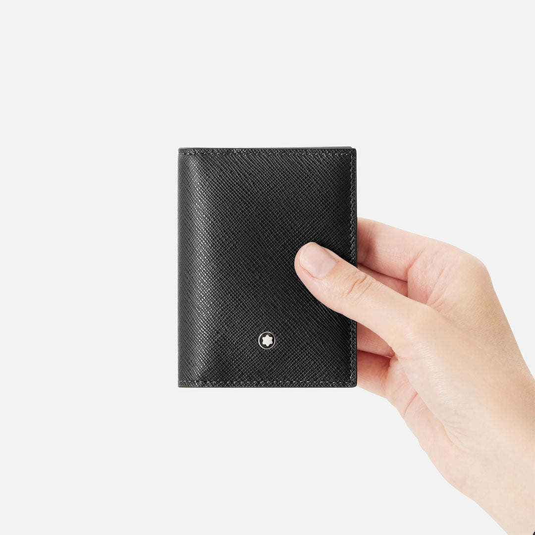 A hand holds the Montblanc Sartorial 4CC Leather Card Holder in black saffiano leather, featuring a small round metallic Montblanc emblem on the front, set against a plain white background.
