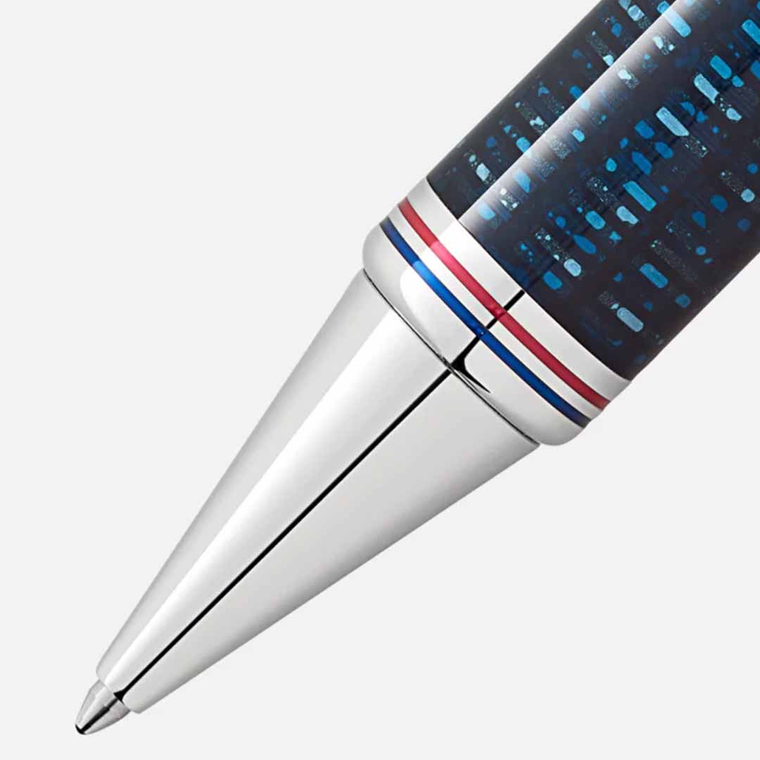 Close-up of the Montblanc Great Characters Homage to The Great Gatsby Special Edition ballpoint pen, featuring a sleek, silver tip and a patterned blue barrel with red, white, and blue ring accents near the tip on a light gray background, reflecting the elegance of The Great Gatsby's Jazz Age.
