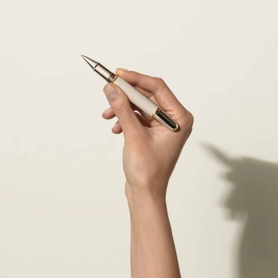 A graceful hand grasps the Montblanc Writers Edition Homage to Jane Austen Limited Edition Rollerball Pen, its silver and gold design standing out against a simple, light background. This evokes the elegance of the Regency era, as if ready to capture timeless words inspired by Jane Austen.