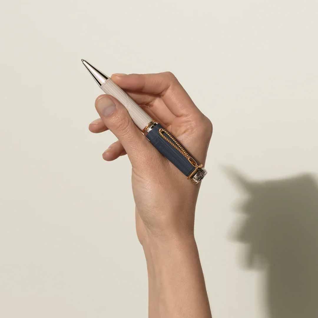 A hand holding the exquisite Montblanc Writers Edition Homage to Jane Austen Limited Edition Ballpoint Pen casts a shadow resembling a playful animal shape on a plain light-colored background, reminiscent of the whimsical creativity found in Jane Austen's Regency era works.