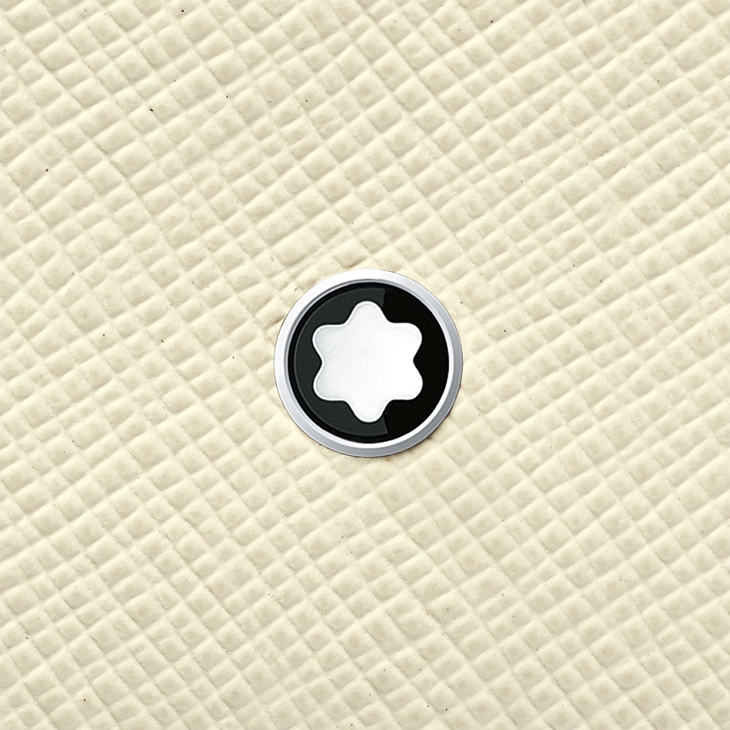 The Montblanc Sartorial Ivory Leather Card Holder features a star-like shape emblem at its center, reminiscent of the iconic Montblanc logo, set against a textured, quilted beige background.