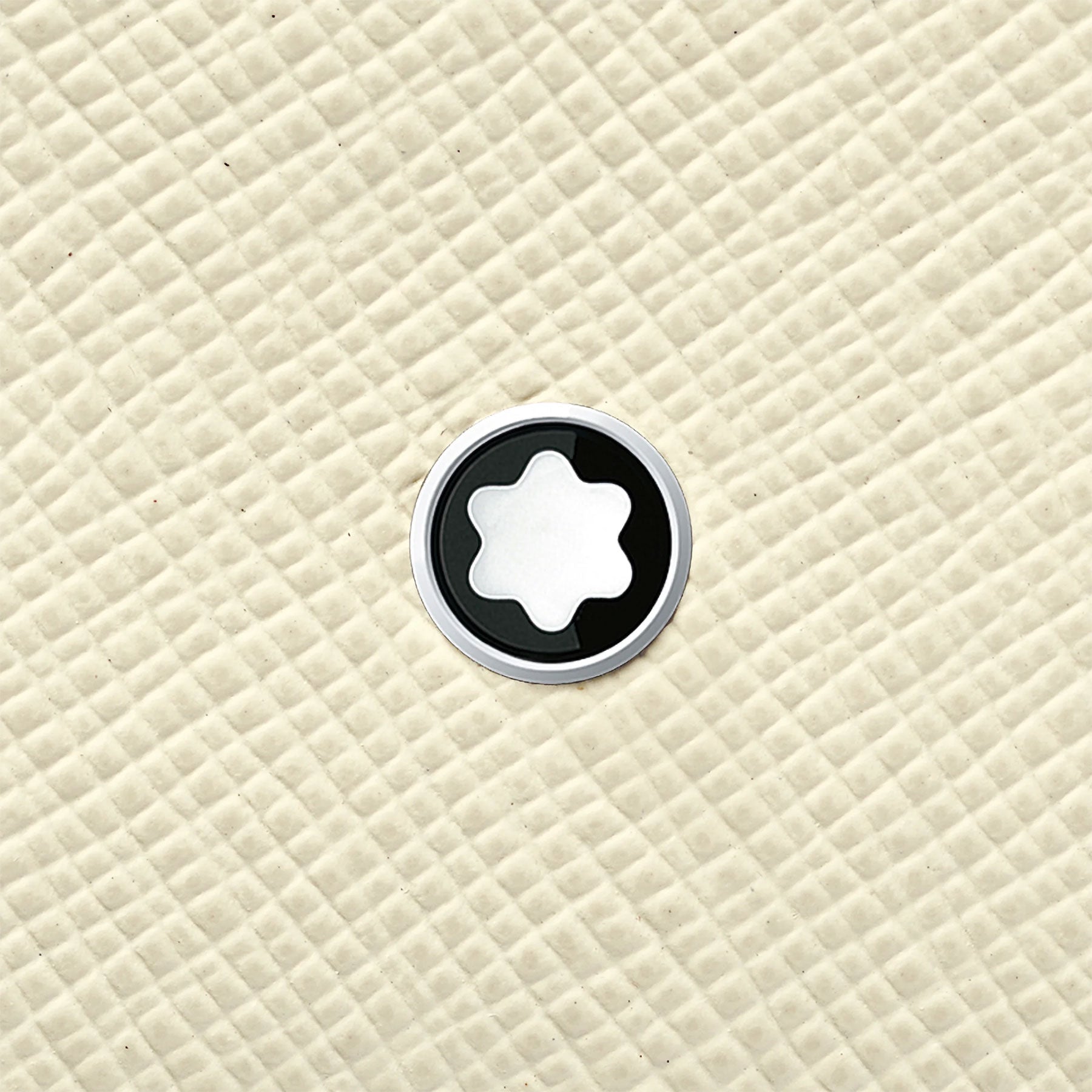 The Montblanc Sartorial Ivory Leather Card Holder features a star-like shape emblem at its center, reminiscent of the iconic Montblanc logo, set against a textured, quilted beige background.