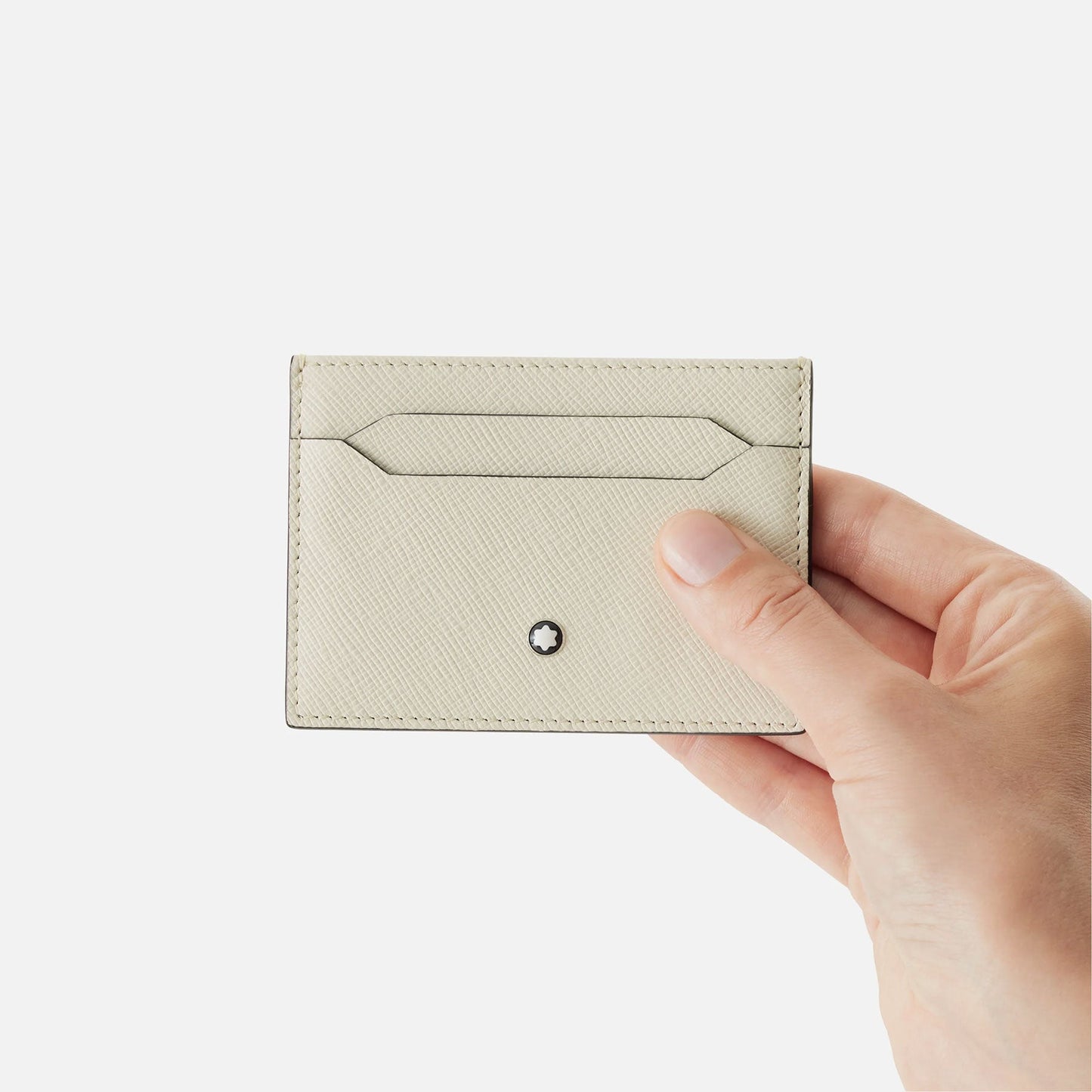 A hand holds the elegant Montblanc Sartorial Ivory Leather Card Holder, made from saffiano-printed leather and proudly displaying the iconic Montblanc emblem. Its minimalist design includes precise stitching and a convenient card slot, all set against a plain white backdrop.