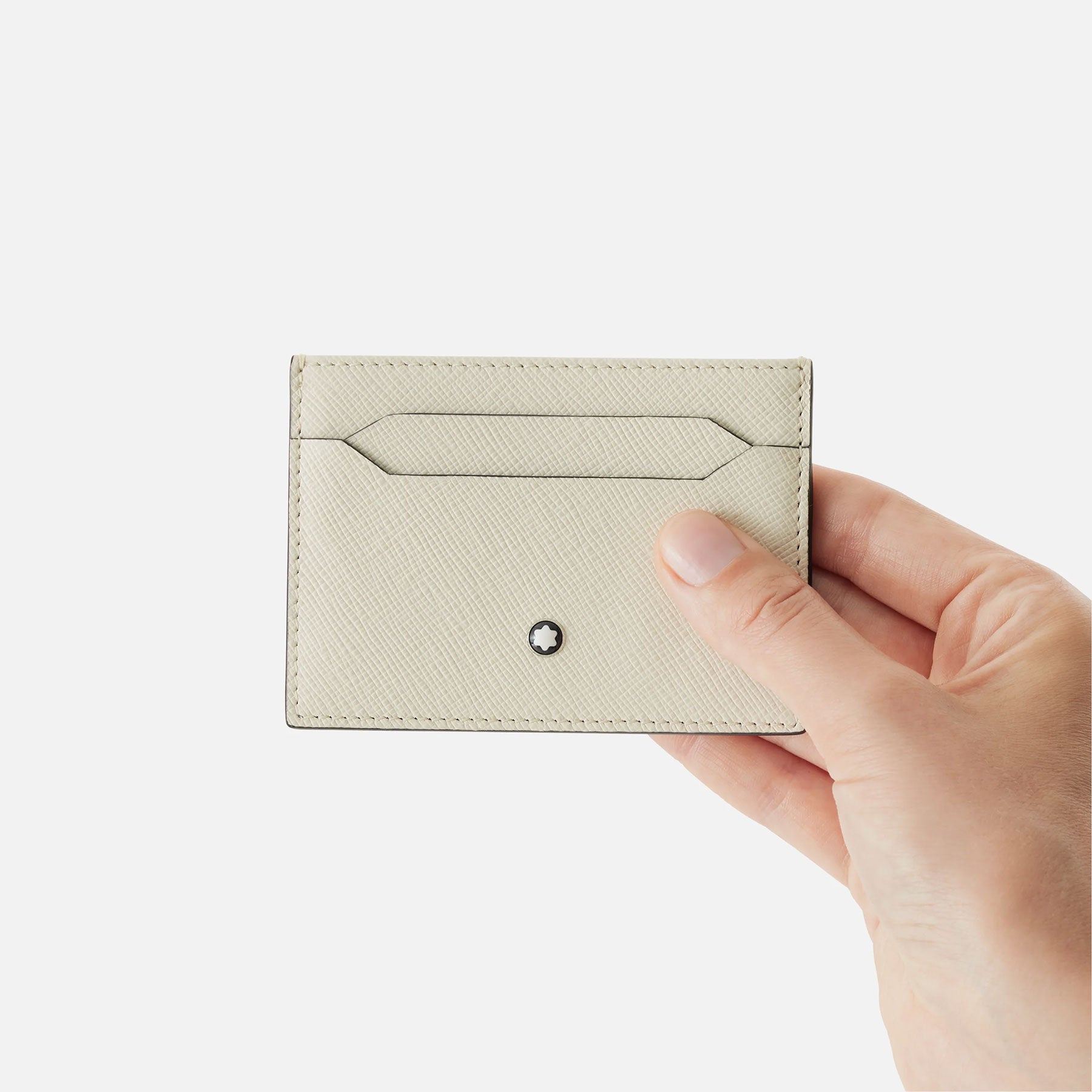 A hand holds the elegant Montblanc Sartorial Ivory Leather Card Holder, made from saffiano-printed leather and proudly displaying the iconic Montblanc emblem. Its minimalist design includes precise stitching and a convenient card slot, all set against a plain white backdrop.