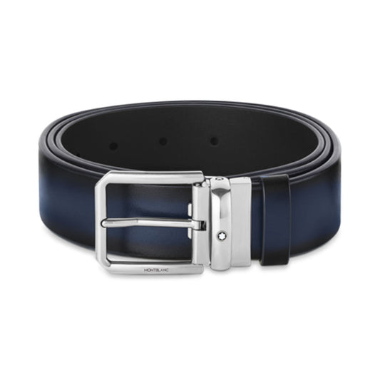 A Montblanc 35mm Black and Blue Reversible Leather Belt with a stainless steel buckle is elegantly coiled. The polished Montblanc emblem on the buckle strikingly stands out, while the belt maintains a simple design without any visible embellishments.