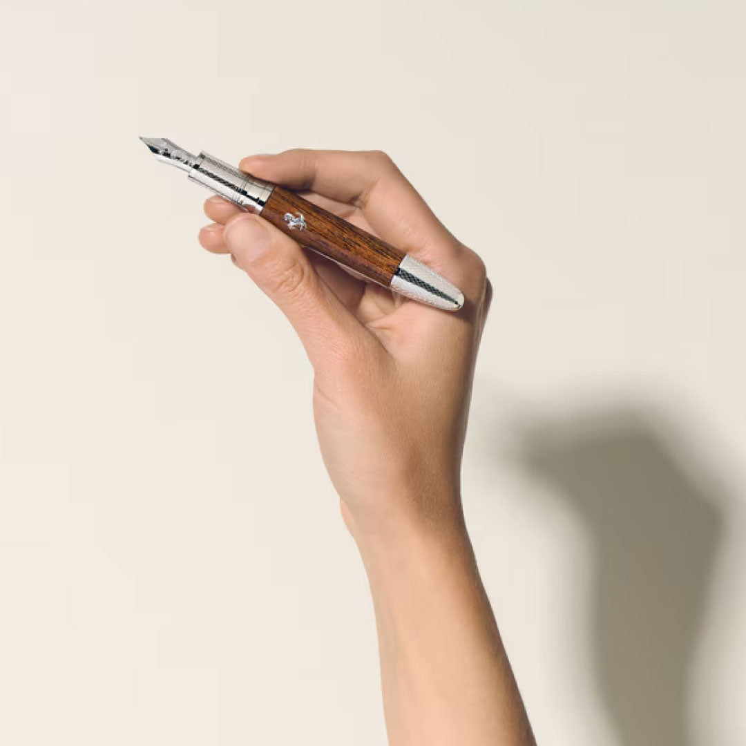 A hand holds a Montblanc Meisterstück Great Masters Ferrari Tailor Made Classica Special Edition Fountain Pen against a plain, light background, casting a subtle shadow.