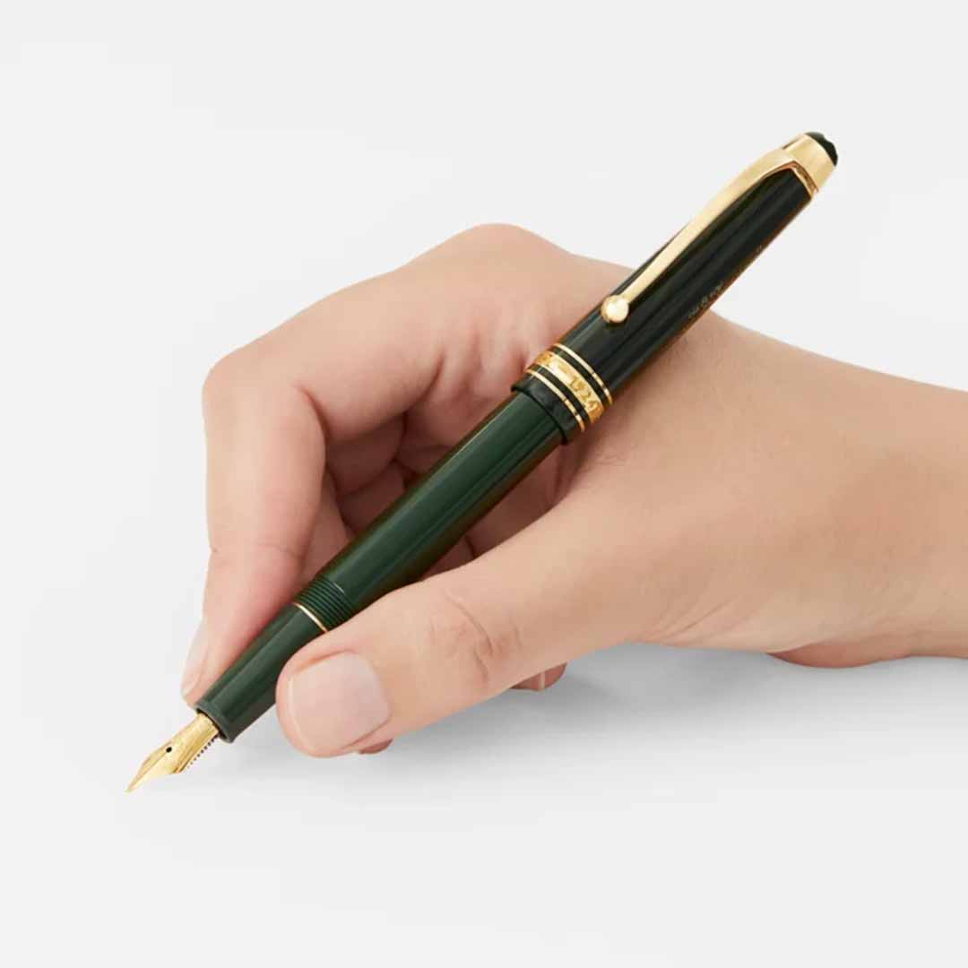 A hand holding the Montblanc Meisterstuck The Origin Collection Classique Fountain Pen, a fine writing instrument with gold accents, against a plain white background.