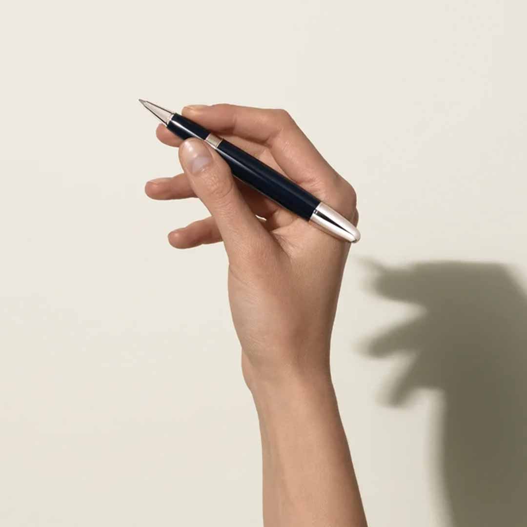 A hand gracefully holds the Montblanc Meisterstück The Origin Collection Doue Le Grand Rollerball Pen against a light background. The fingers elegantly curve around the instrument, casting a subtle shadow on the surface behind.