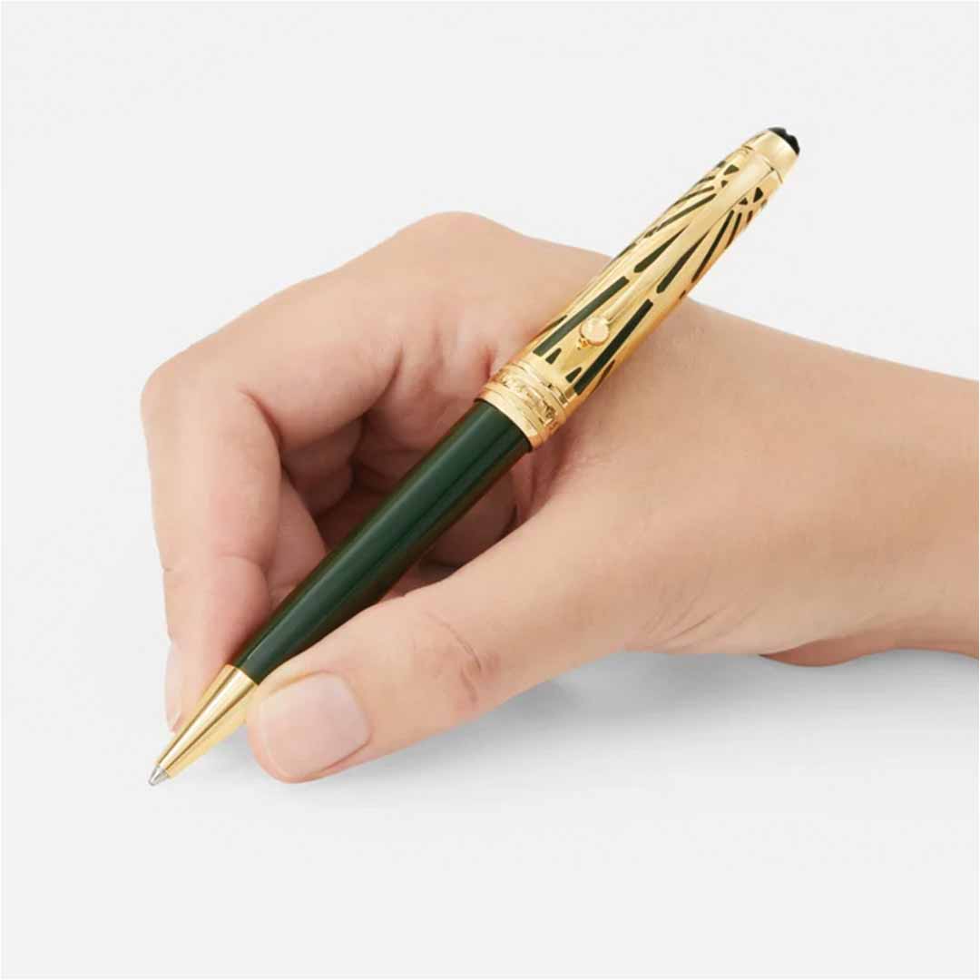 A hand holding the Montblanc Meisterstück The Origin Collection Doue Classique Ballpoint Pen, featuring a dark green barrel with gold accents and an Art Déco inspired design, is poised to write on a plain white surface.