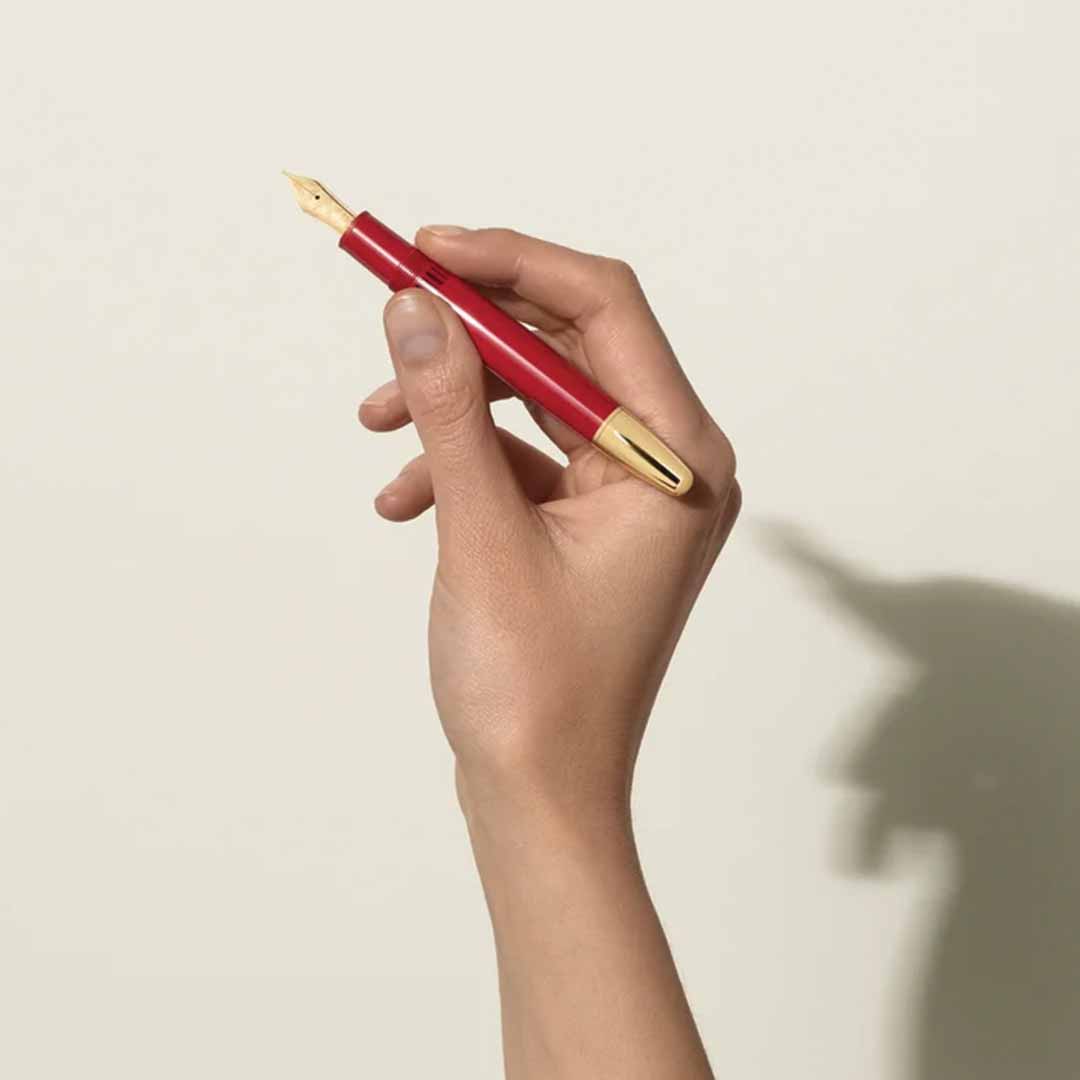 A hand holding a Montblanc Meisterstück X Olympic Heritage Paris 1924 LeGrand Fountain Pen casts a shadow on a light-colored wall, resembling a unicorn with a horn and capturing the elegance synonymous with Montblanc's craftsmanship.