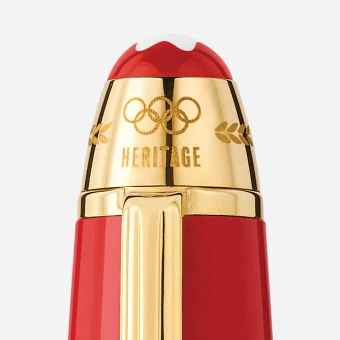 A close-up of the Montblanc Meisterstück X Olympic Heritage Paris 1924 Le Grand Fountain Pen showcases its red body with a white tip and gold accents. This special edition features engraved Olympic rings and "HERITAGE" in gold, adorned with leaf motifs, and is distinguished by its handcrafted gold nib.
