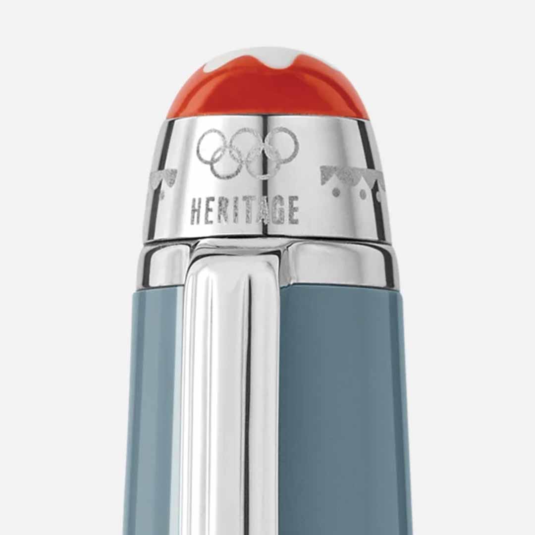 Close-up of the cap from the Montblanc Meisterstück X Olympic Heritage Chamonix 1924 Classique Rollerball Pen, showcasing a silver top with an orange and white design. The cap is elegantly engraved with "HERITAGE" and interlocking rings, commemorating the Meisterstück centenary. The pen's light blue body is adorned with shiny metallic accents.