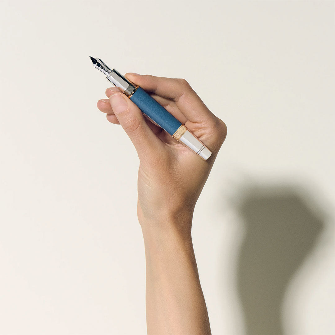 A hand holds the Montblanc Writers Edition Homage to Johann Wolfgang von Goethe Limited Edition Fountain Pen upright against a light background, its blue and silver design casting a soft shadow and echoing German literary heritage.