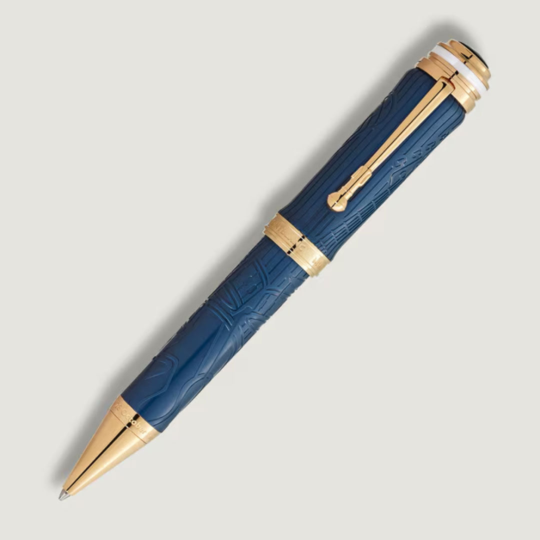 A Montblanc Great Characters Homage to Queen Special Edition ballpoint pen with engraved patterns and gold accents lies diagonally on a light gray background.