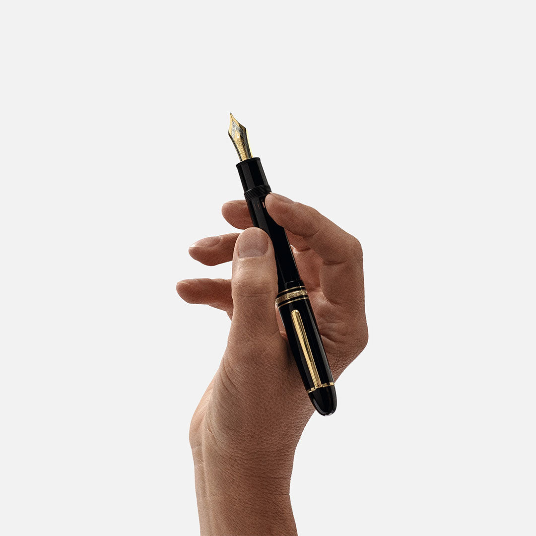 A hand holds the Montblanc Meisterstuck Yellow Gold Coated 149 Fountain Pen, featuring a gleaming gold nib and elegant gold accents, against a plain white background.