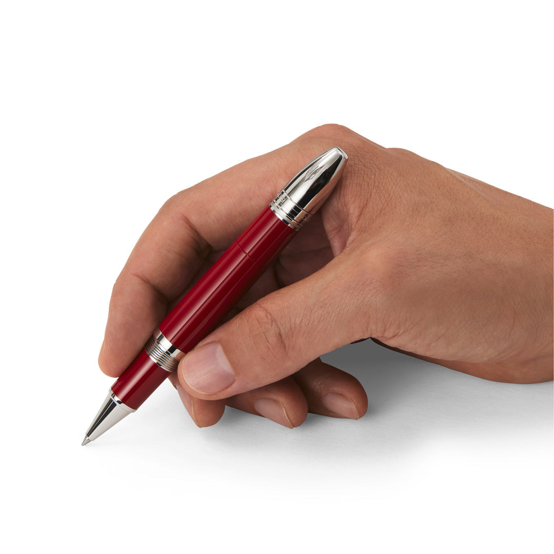 A hand holding the Montblanc Great Characters Enzo Ferrari Special Edition Rollerball Pen, featuring striking red and silver accents, is poised above a white surface as if ready to write.
