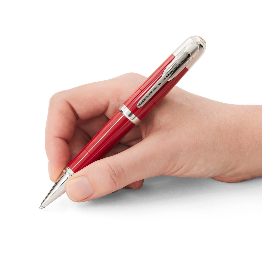 A hand holding the Montblanc Great Characters Enzo Ferrari Special Edition Ballpoint Pen by Montblanc, its striking red and silver design poised above a white surface.