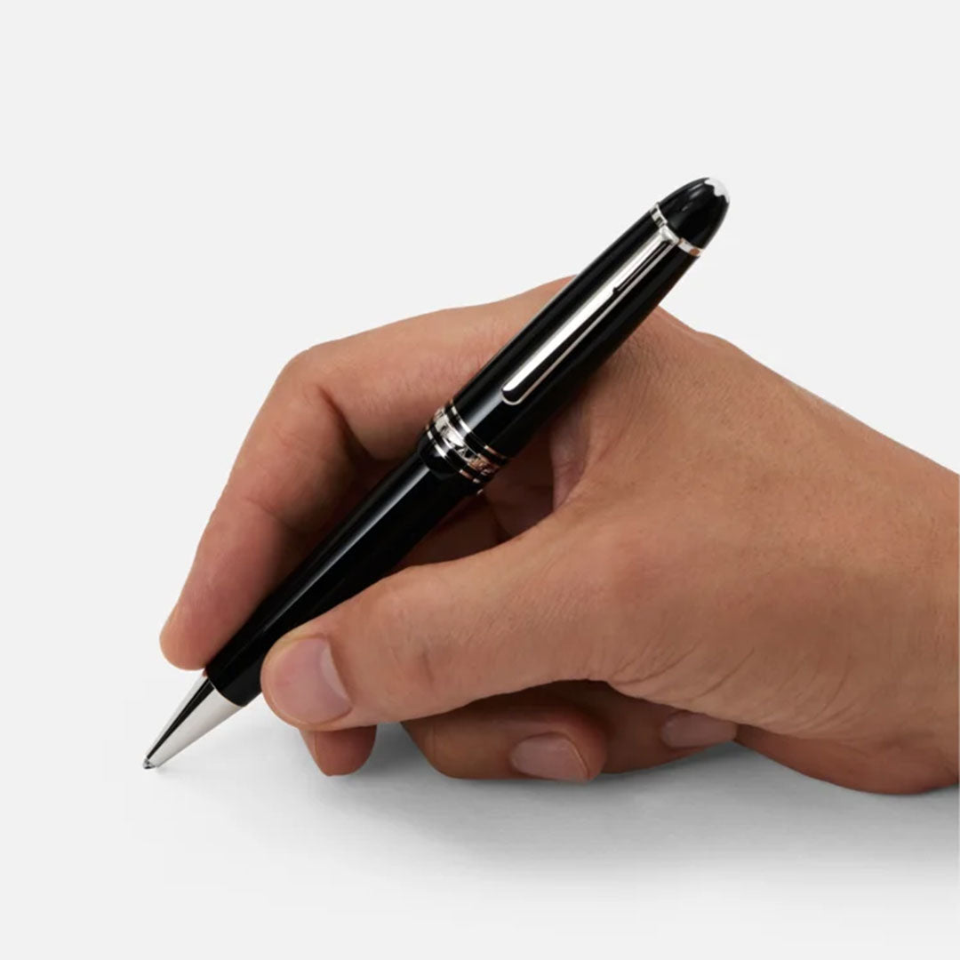 A hand holds a Montblanc Meisterstuck Platinum Coated Legrand Ballpoint Pen above a blank white surface, ready to write.