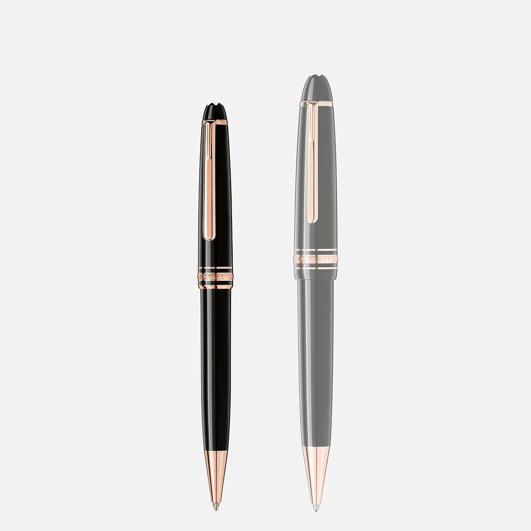 Two Montblanc Meisterstück Rose Gold Coated Ballpoint Pens, one partially transparent and one fully opaque, stand upright on a plain light gray background, showcasing the luxury and timeless design of Montblanc writing instruments.
