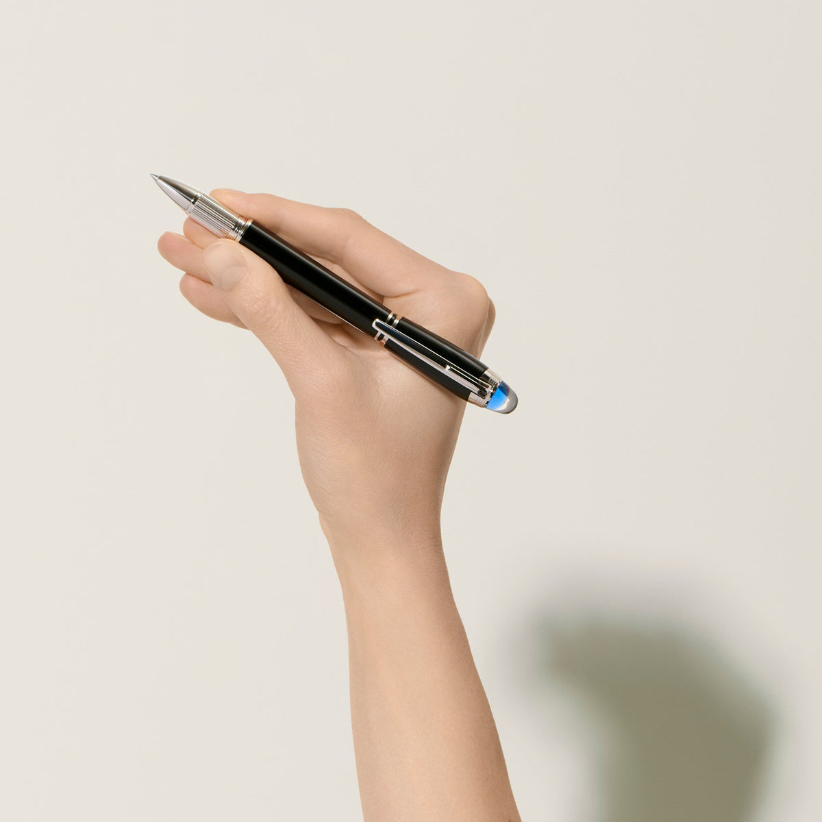 A hand holds a black Montblanc StarWalker Precious Resin Fineliner Pen with silver accents and a translucent blue dome on the end.