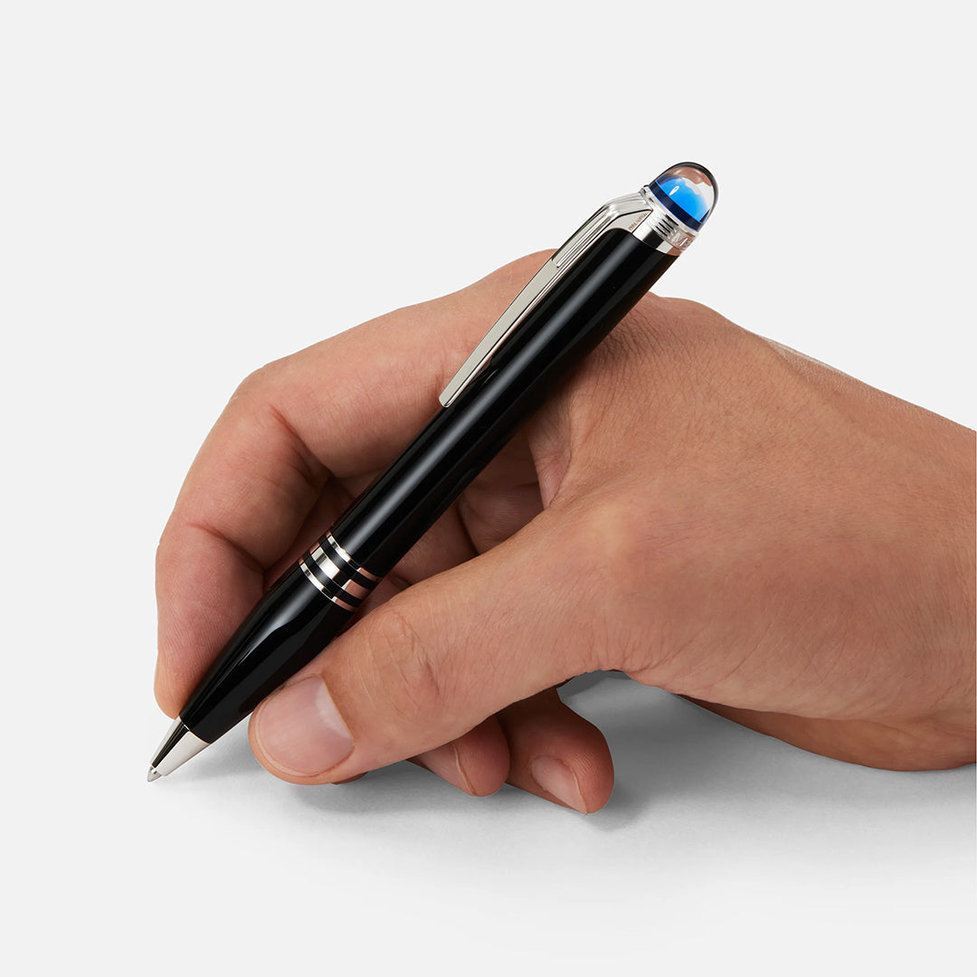 A hand holds a Montblanc Starwalker Precious Resin Ballpoint Pen with a silver clip and blue tip, poised above a blank white surface.