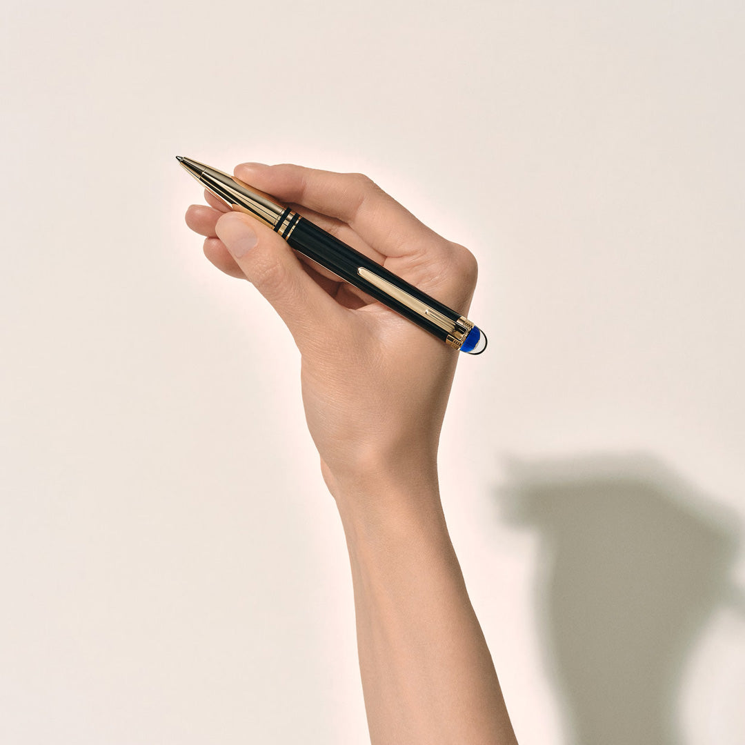 A hand holding a Montblanc StarWalker Doue Ballpoint Pen by Montblanc against a plain light background, with the pen tip pointing upward and a faint shadow to the right, evoking subtle inspiration from space exploration.