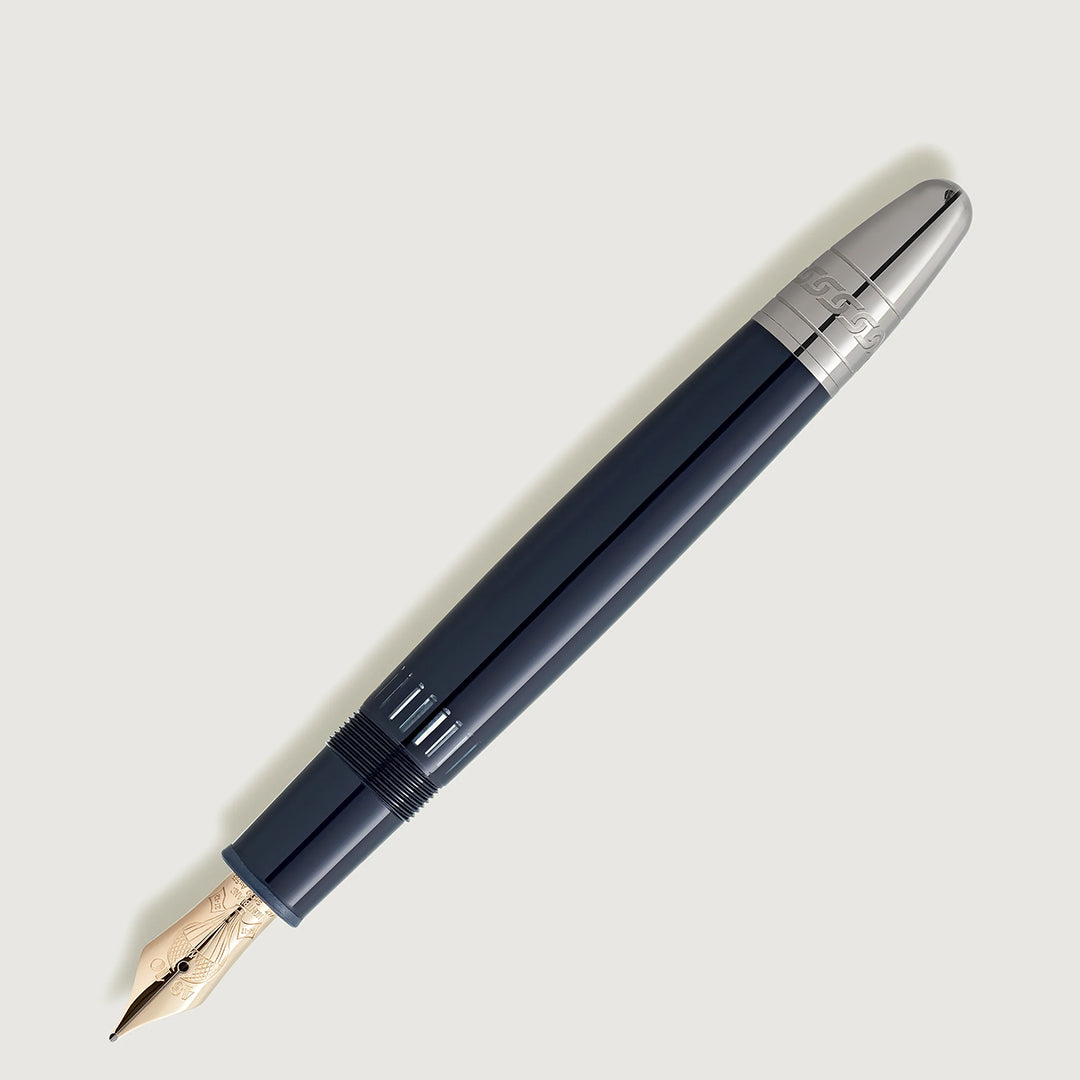 The Montblanc Meisterstuck Around the World in 80 Days LeGrand Fountain Pen, crafted from dark blue precious resin with silver accents, sits diagonally on a light background. The uncapped pen reveals a gold nib with intricate engravings inspired by a Jules Verne adventure.
