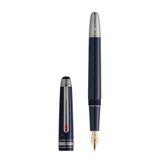 A blue Montblanc Meisterstück Around the World in 80 Days Classique Fountain Pen with silver accents stands vertically, its cap featuring a red heart detail and geometric-patterned silver clip. The gold nib contrasts elegantly with the blue body, echoing Jules Verne's adventurous spirit.