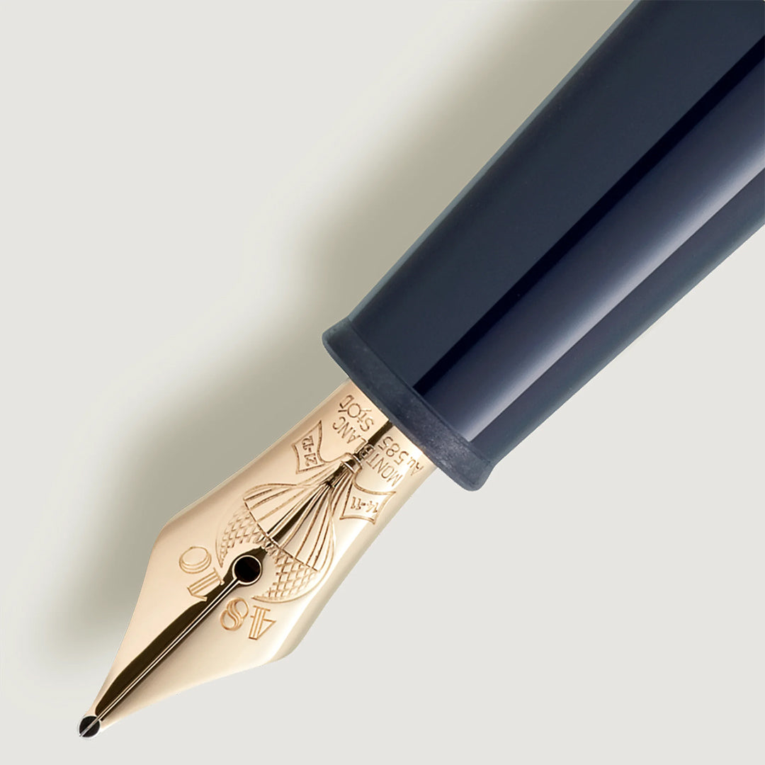 The Montblanc Meisterstuck Around the World in 80 Days Classique Fountain Pen features a gold-colored nib with intricate engravings, including "18K" and "750," evoking Jules Verne's adventurous spirit. It connects to a dark, glossy barrel and rests diagonally on a light, neutral background.