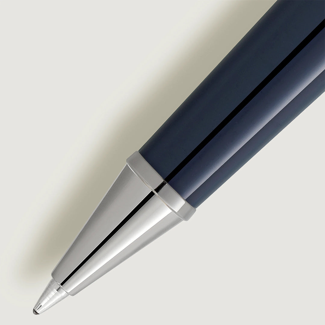 The Montblanc Meisterstück Around the World in 80 Days Classique Rollerball Pen rests diagonally on a light gray background, displaying its sleek metallic tip and dark blue barrel, accentuating its smooth and shiny design.