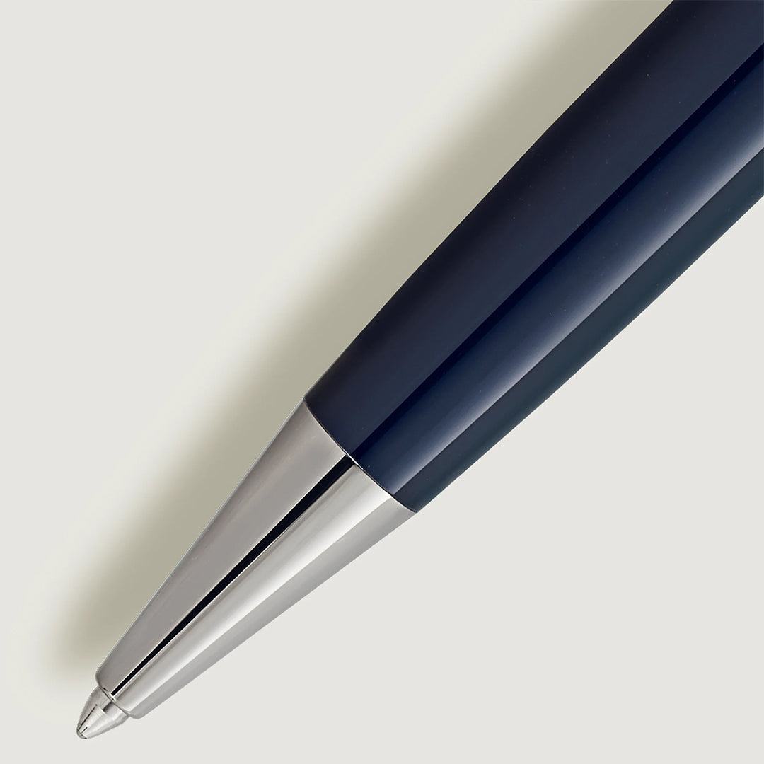 The diagonal close-up highlights the Montblanc Meisterstuck "Around the World in 80 Days" Classique Ballpoint Pen with its dark barrel and sleek metallic tip against a light background, emphasizing its shiny silver tip and smooth, dark body.