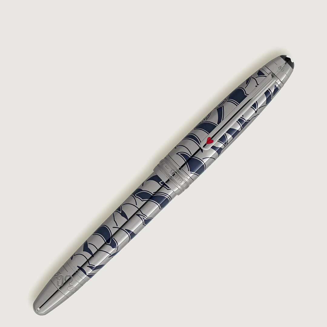 The Montblanc Meisterstück Around the World in 80 Days Solitaire LeGrand Rollerball Pen, featuring blue wave patterns and a small red heart on the cap, is displayed diagonally against a light gray background.