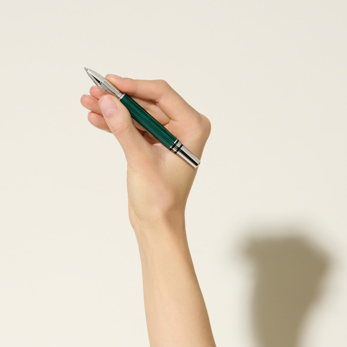 A hand holds a Montblanc StarWalker PolarGreen Doue Fineliner Pen upright against a light background, casting its shadow on the wall.