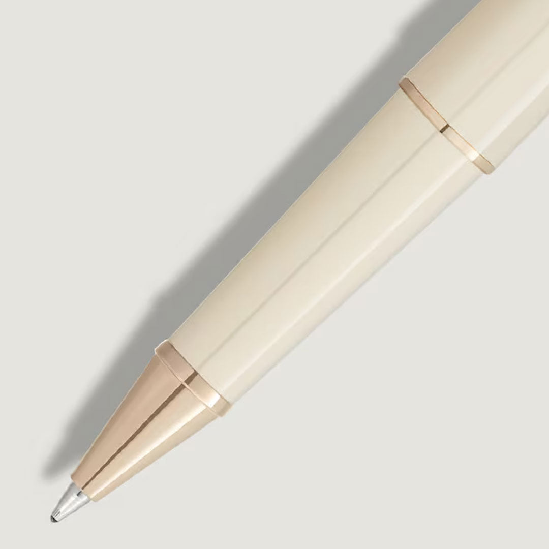 A close-up of the Montblanc Meisterstuck Romeo & Juliet Classique Rollerball Pen in beige precious resin with gold accents is shown diagonally on a light gray background, its tip casting a faint shadow.