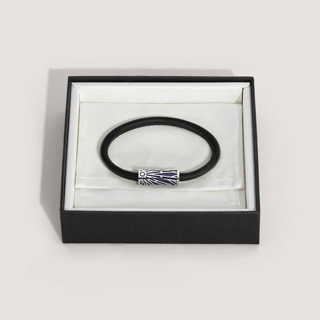The Montblanc Meisterstuck Origins Blue Leather Bracelet, featuring a decorative silver clasp, is elegantly nestled in a white padded jewelry box with a sleek black exterior.