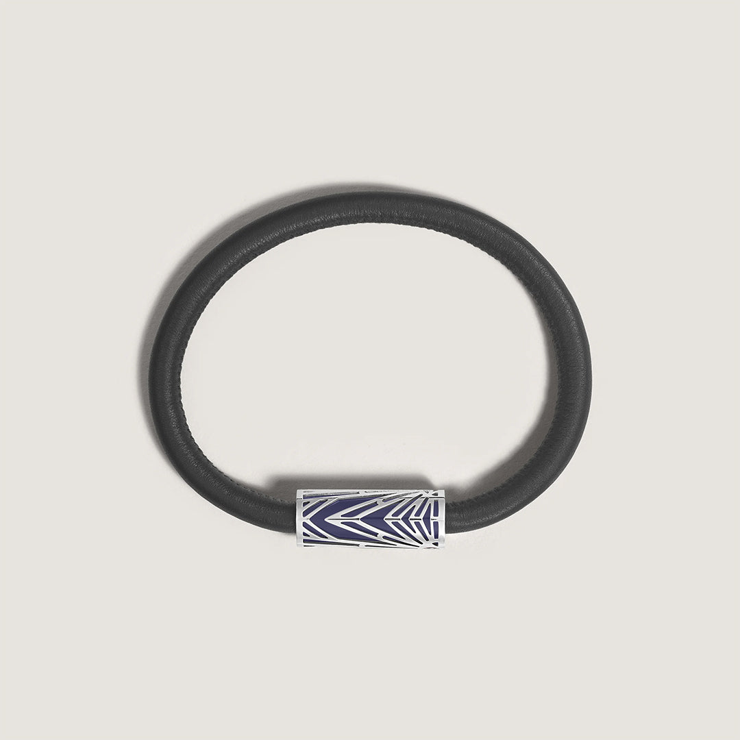 The Montblanc Meisterstuck The Origin Collection Leather Bracelet features a black leather band with a silver clasp adorned with an abstract geometric pattern, set against a light grey backdrop. Its refined design is accentuated by durable, modern stainless steel detailing.