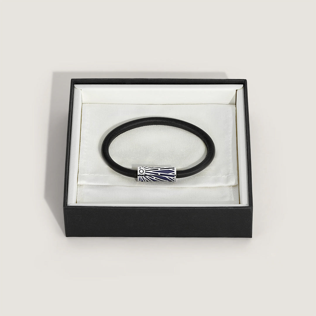 The Montblanc Meisterstuck The Origin Collection Leather Bracelet, in sleek black leather with a silver charm engraved with a sunburst design, is elegantly showcased in an open black and white jewelry box, making it the perfect accent for any ensemble.