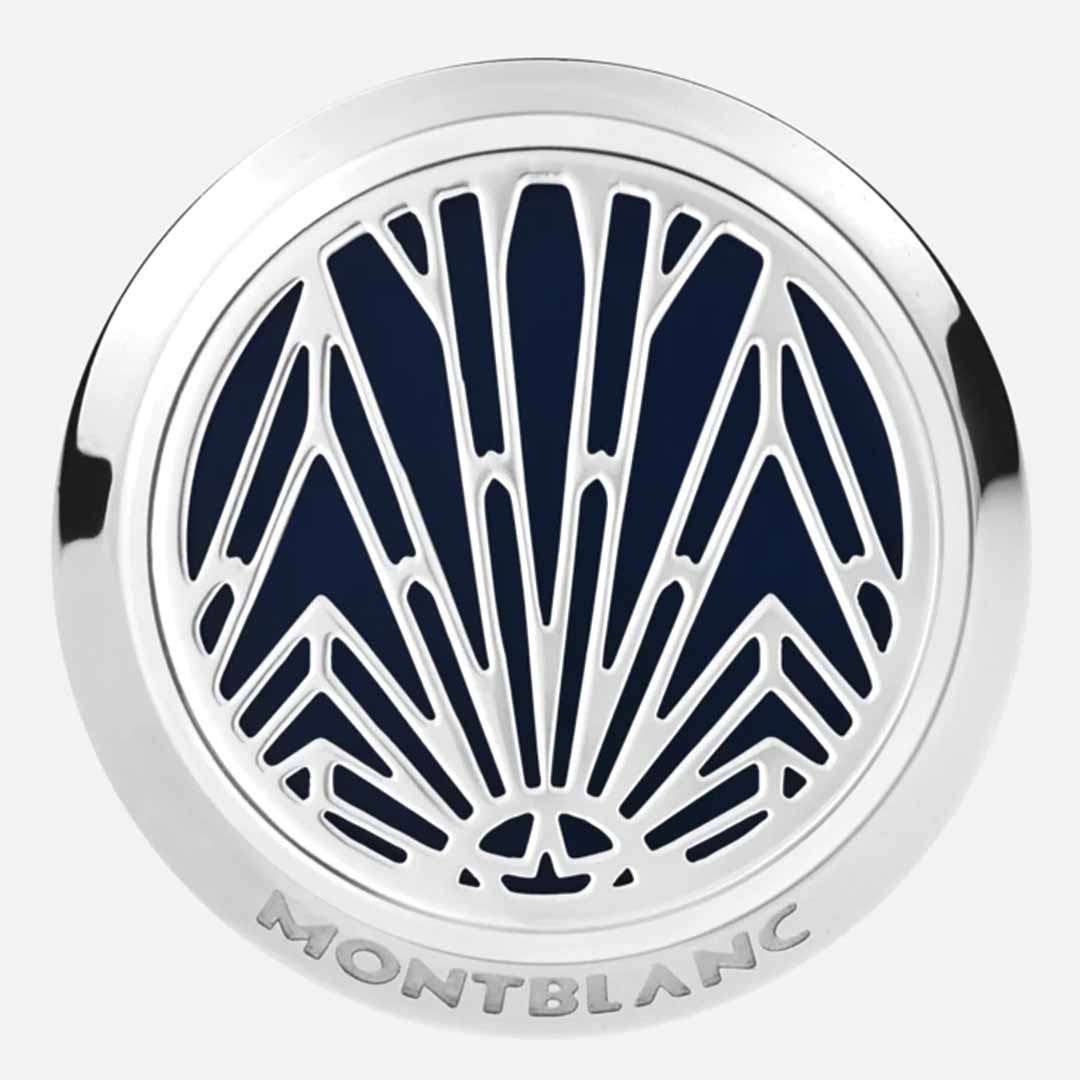 A close-up of a round silver lid showcases an intricate geometric pattern in dark blue and silver, reminiscent of the elegance found in Montblanc Meisterstück designs. The word "MONTBLANC" is engraved at the bottom edge, mirroring the sophistication of Montblanc Meisterstück The Origin Collection Blue Cufflinks.