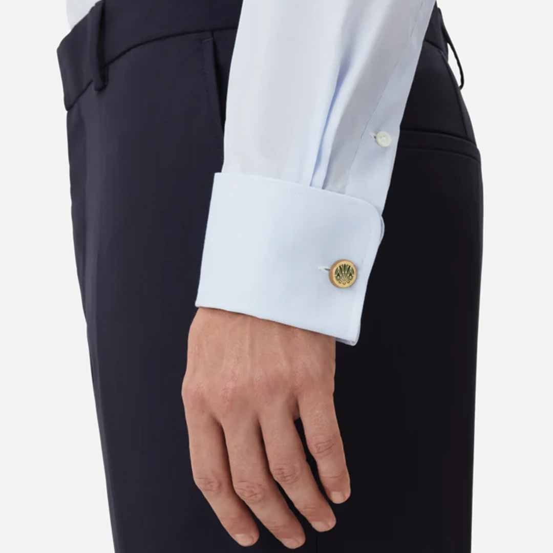 A person is wearing a light blue dress shirt with French cuffs, highlighted by the elegant Montblanc Meisterstuck The Origin Collection Green Cufflinks, which feature a striking green lacquer inlay. Although they are also wearing dark trousers, the exquisite sleeve and cufflink detail remains the main focus.