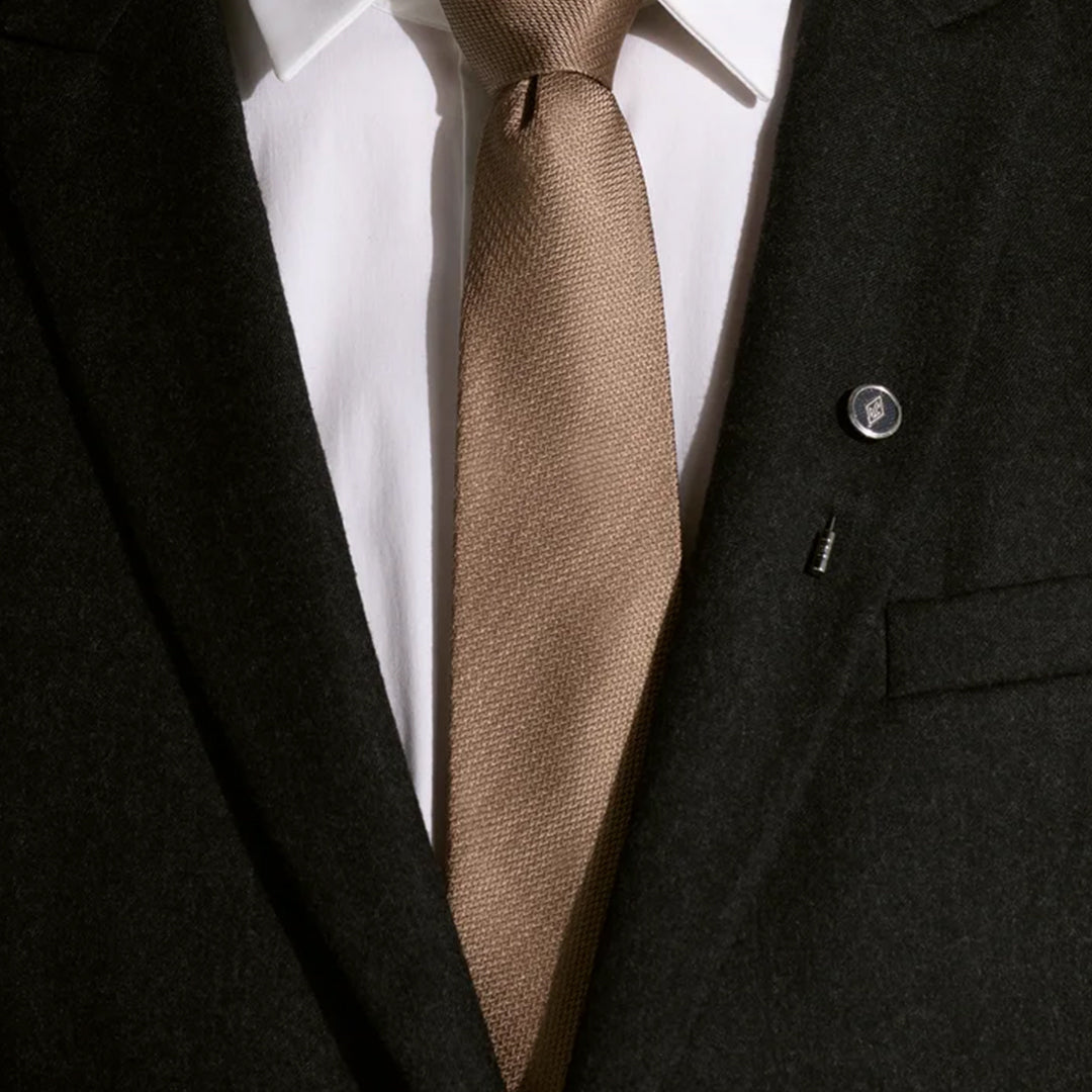 Close-up of a person wearing a dark suit with a white shirt and brown tie, showcasing the Montblanc Great Characters Homage To The Great Gatsby lapel pin on the lapel, capturing Gatsby's timeless elegance.