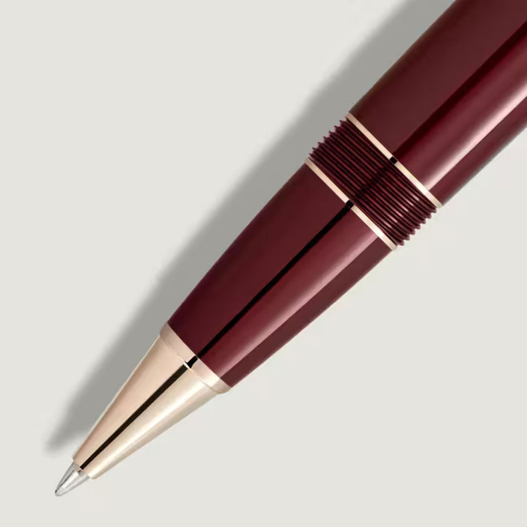 A close-up of a Montblanc Meisterstück Burgundy Red Legrand Rollerball Pen with gold accents, shown pointing downwards on a plain light gray background.