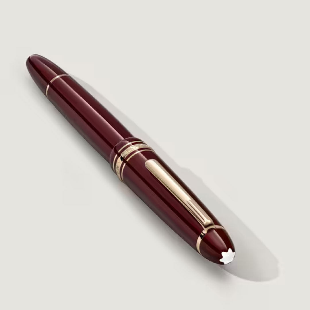 A Montblanc Meisterstück Burgundy Red LeGrand Rollerball Pen by Montblanc, featuring elegant gold accents and the iconic white star emblem on the cap, is displayed on a light gray background.