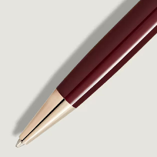 Close-up of a Montblanc Meisterstuck Burgundy Red Classique Ballpoint Pen with gold trim, displayed diagonally on a light gray background.