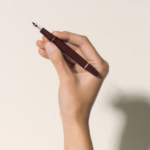 A hand holds a Montblanc Meisterstück Burgundy Red Classique Fountain Pen with gold fittings against a plain, light background.