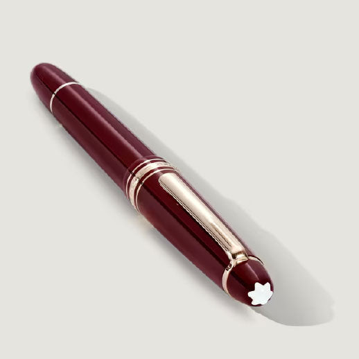 The Montblanc Meisterstück Burgundy Red Classique Fountain Pen, featuring gold fittings and a white star emblem on the cap, is displayed diagonally on a light grey background.