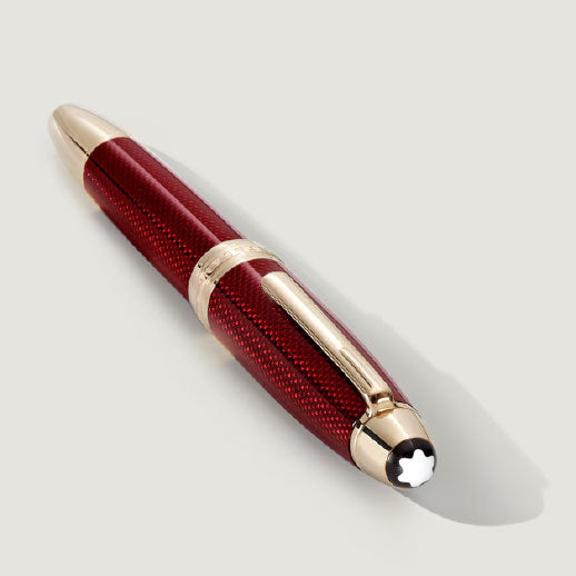 A Montblanc Meisterstück Solitaire Golden Hour Rollerball Pen is shown on a light grey surface, featuring a textured burgundy red lacquer barrel, gold-coated accents, and the iconic white star emblem on its cap.