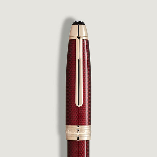 A close-up of the Montblanc Meisterstück Solitaire Golden Hour Rollerball Pen, highlighted in burgundy red lacquer with gold-toned fittings and a textured barrel, displayed vertically on a plain light background.