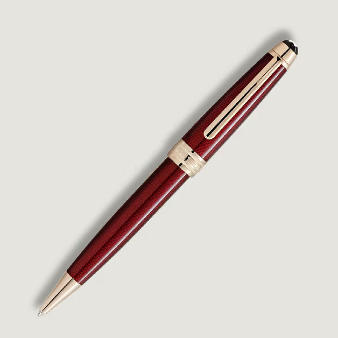 The Montblanc Meisterstück Solitaire Golden Hour Ballpoint Pen, featuring a burgundy red lacquer and gold-coated accents, is shown diagonally against a plain light background.